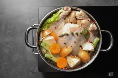 Photo of Whole fresh turkey, cut onion, carrot, celery, spices in pot and stove on grey textured table, top view