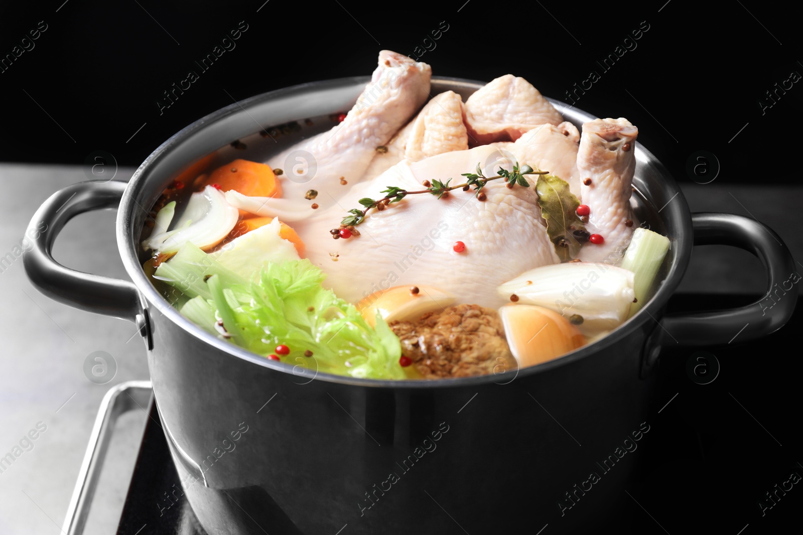 Photo of Whole fresh turkey, cut onion, celery, spices in pot and stove on table against black background, closeup