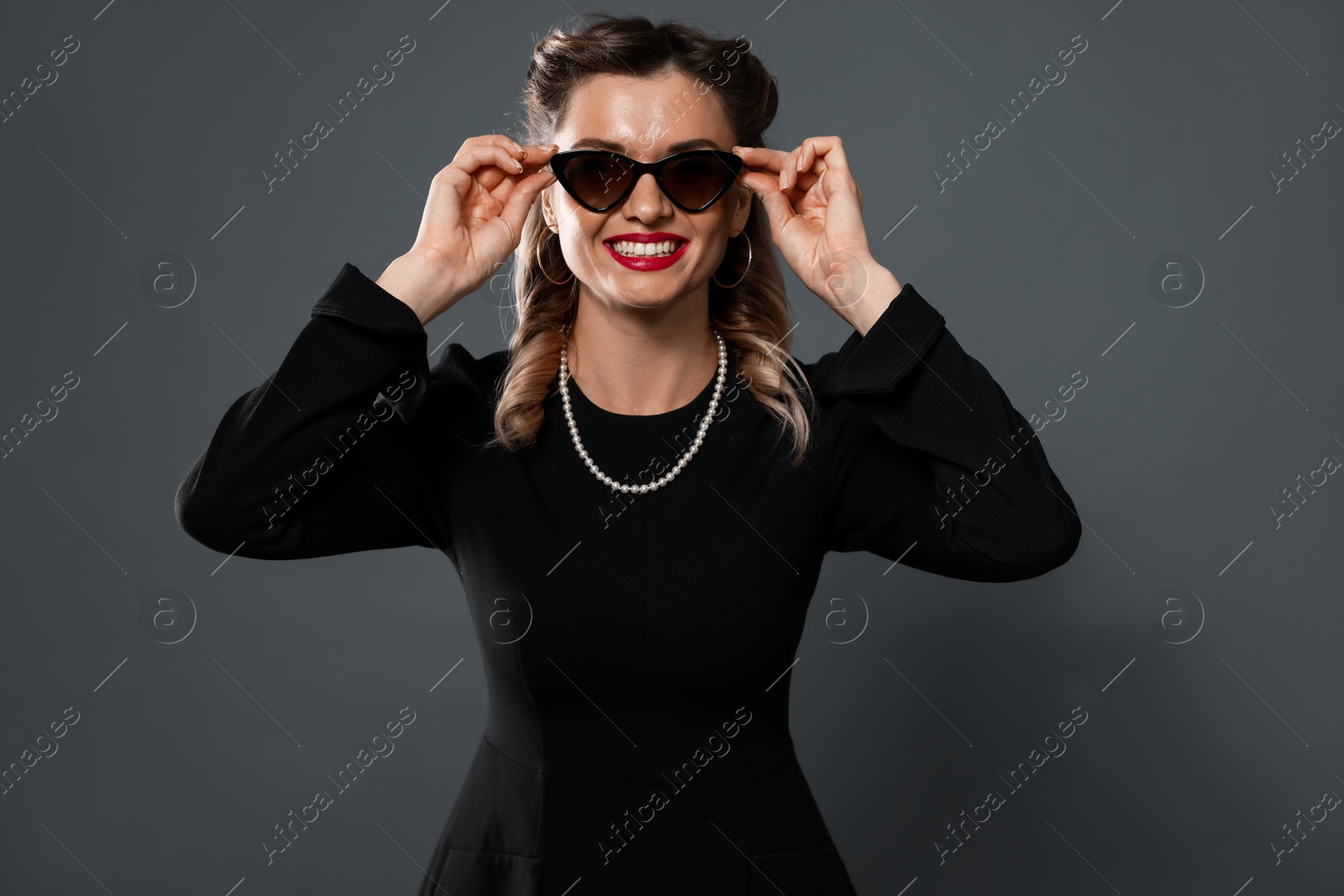 Photo of Happy woman in sunglasses on grey background. Pin-up vibe portrait