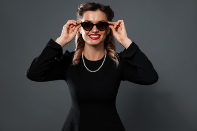 Photo of Happy woman in sunglasses on grey background. Pin-up vibe portrait