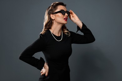 Beautiful woman in sunglasses on grey background. Pin-up vibe portrait