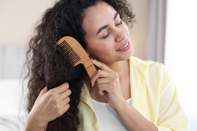 Smiling young woman brushing her curly hair with comb at home