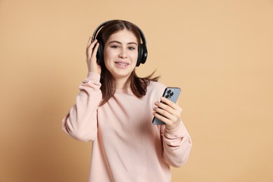 Photo of Portrait of teenage girl in headphones with smartphone on beige background