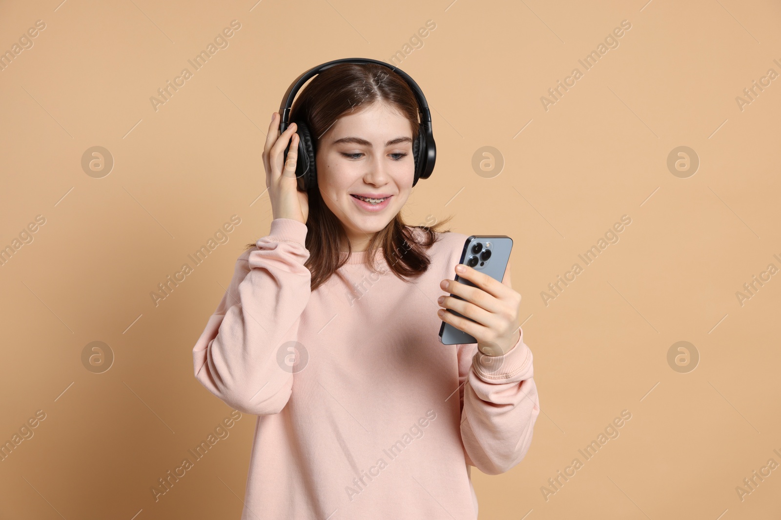 Portrait of teenage girl in headphones with smartphone on beige background Photo of Portrait of teenage girl in headphones with smartphone on beige background