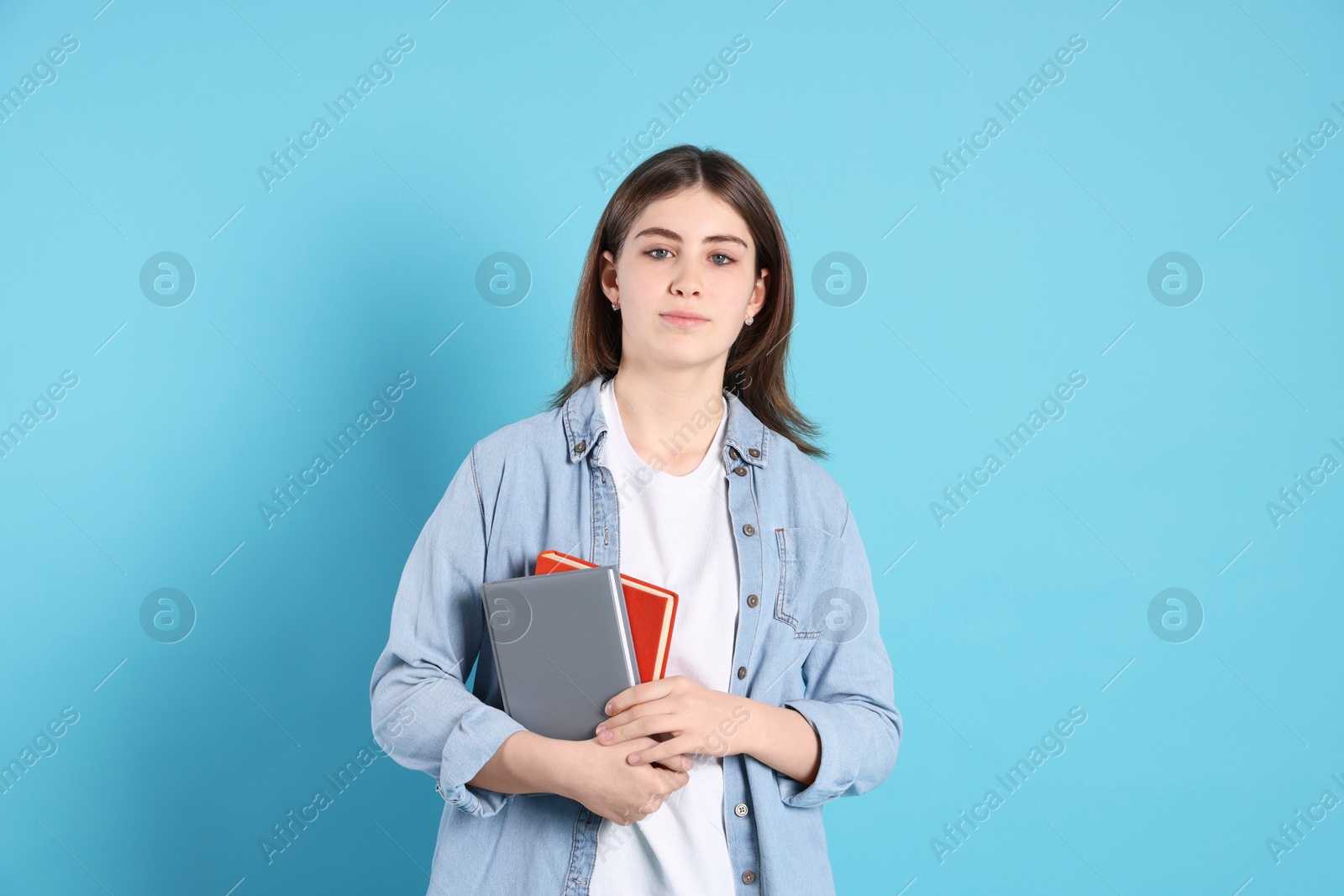 Photo of Portrait of teenage girl with books on light blue background