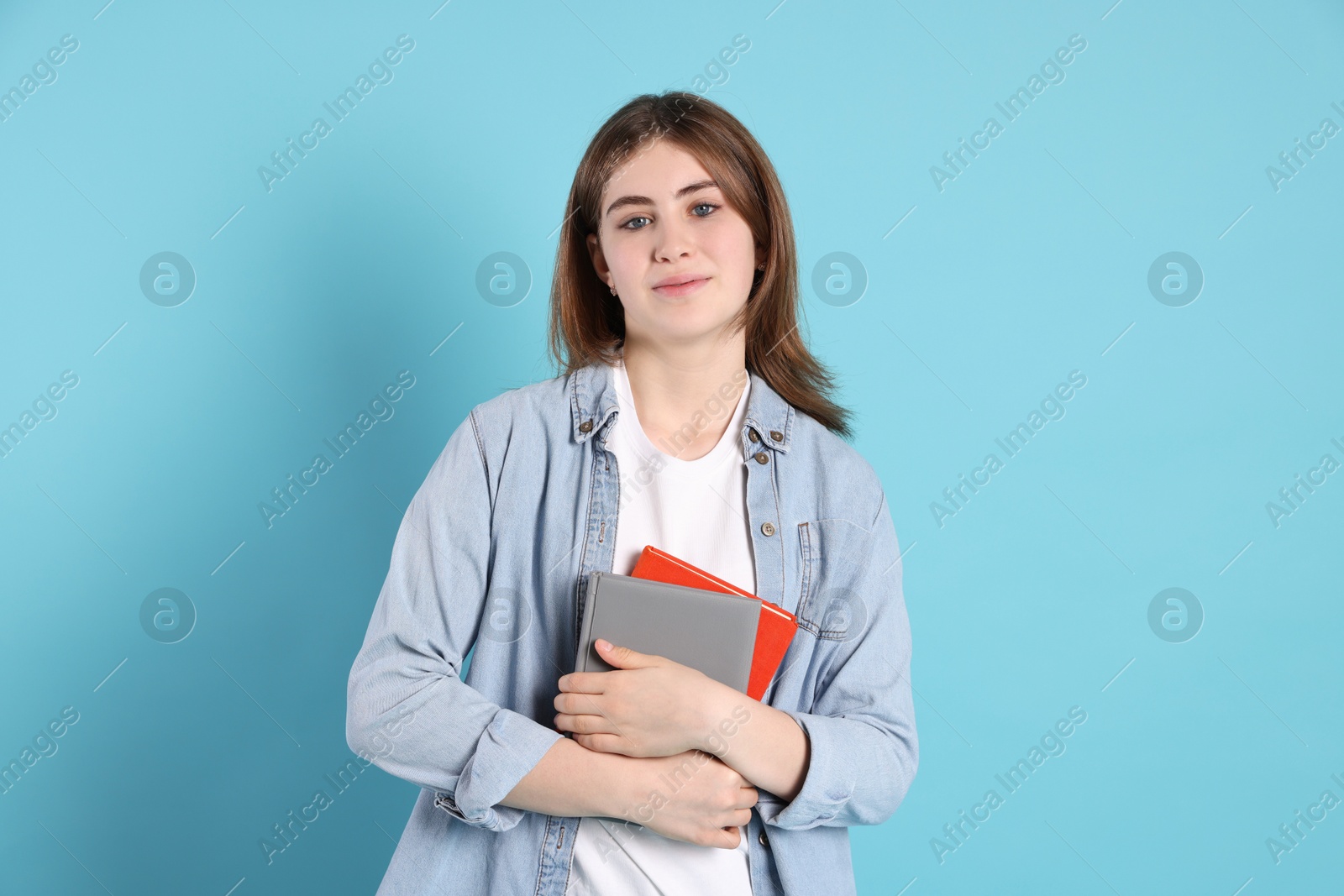 Photo of Portrait of teenage girl with books on light blue background