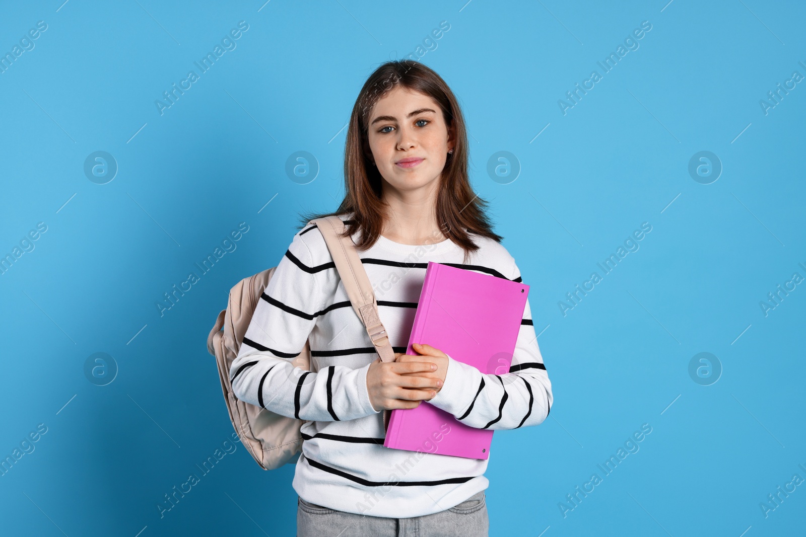 Photo of Portrait of teenage girl with backpack and folder on light blue background