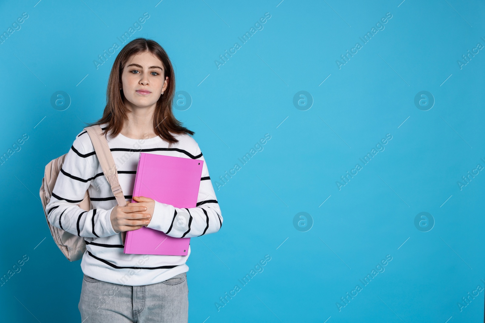 Photo of Portrait of teenage girl with backpack and folder on light blue background. Space for text