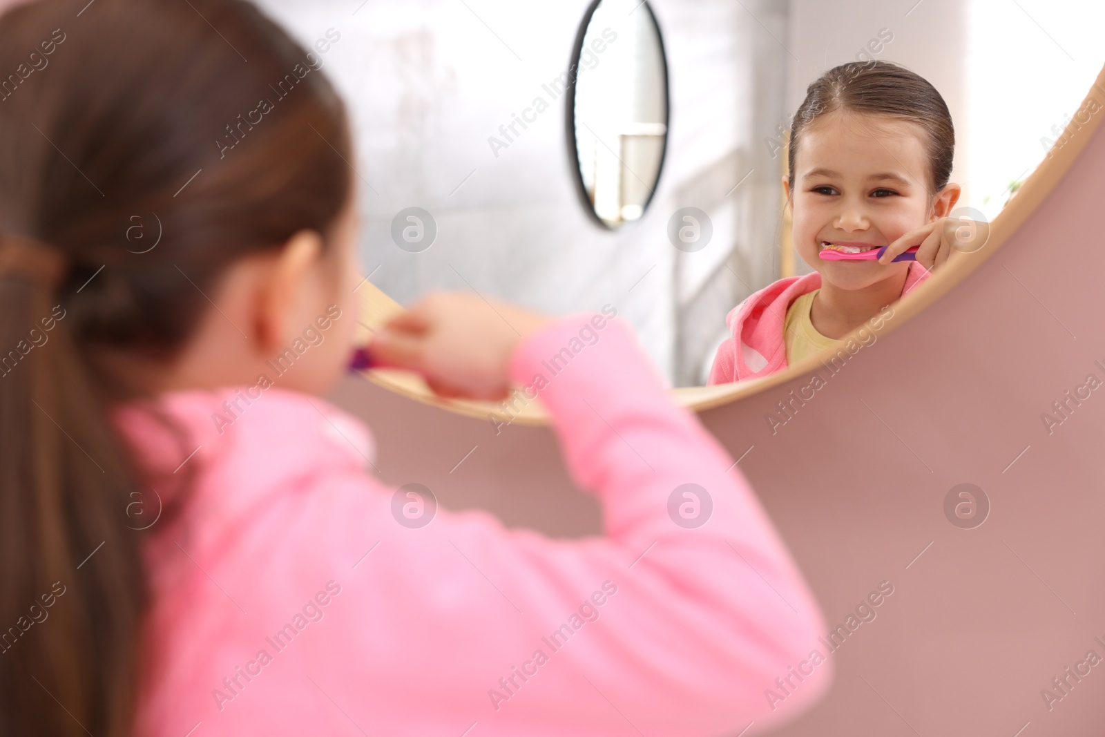 Photo of Cute girl brushing her teeth near mirror in bathroom, selective focus