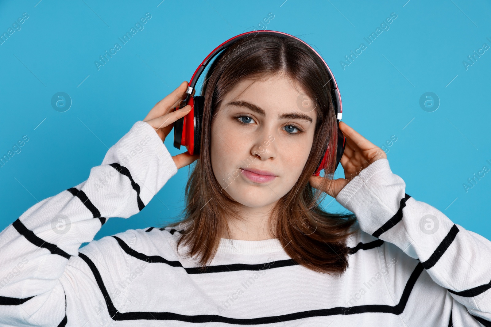 Photo of Portrait of teenage girl in headphones listening to music on light blue background