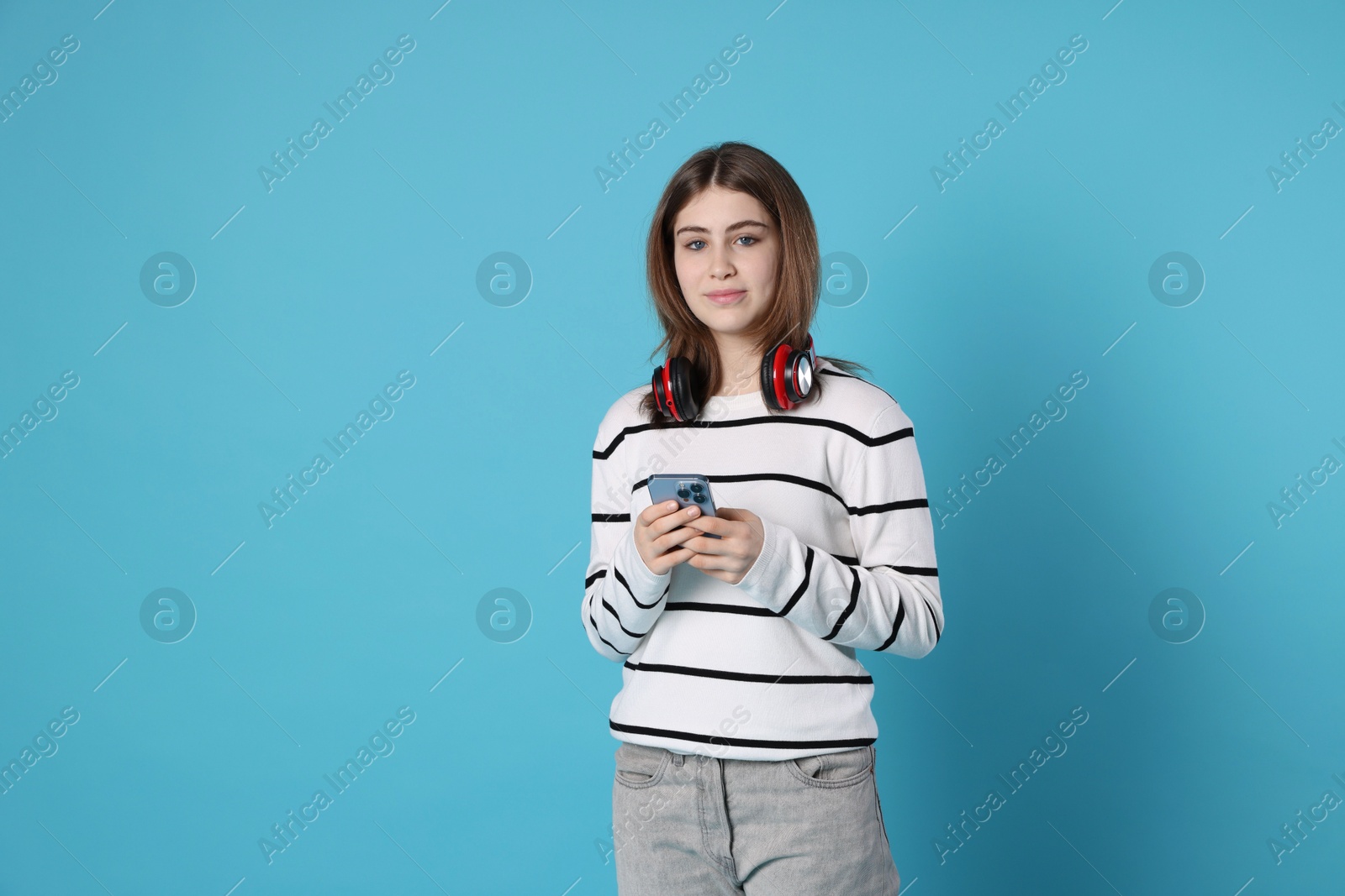 Photo of Portrait of teenage girl with headphones and smartphone on light blue background. Space for text