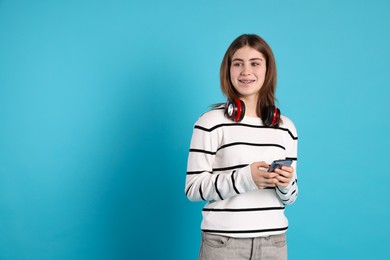 Photo of Portrait of teenage girl with headphones and smartphone on light blue background. Space for text