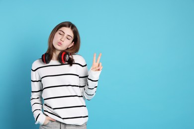 Photo of Portrait of teenage girl with headphones showing V-sign on light blue background. Space for text