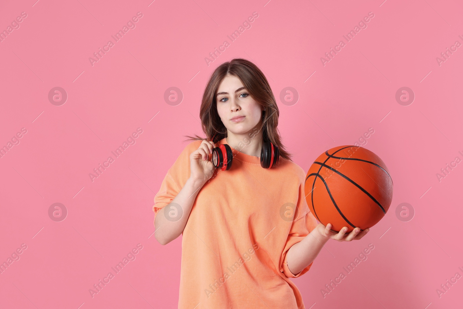 Photo of Portrait of teenage girl with headphones and basketball ball on pink background