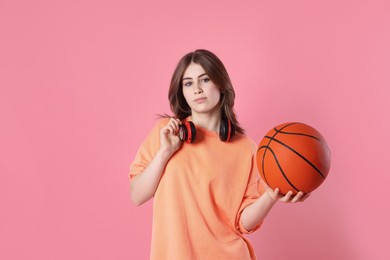 Photo of Portrait of teenage girl with headphones and basketball ball on pink background