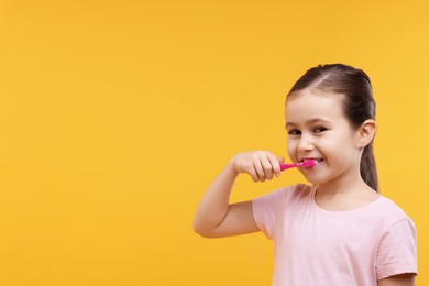 Photo of Cute girl brushing her teeth on orange background, space for text