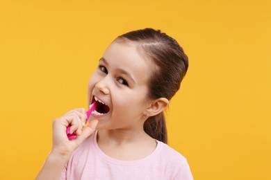 Photo of Cute girl brushing her teeth on orange background