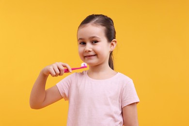 Photo of Cute girl with toothbrush on orange background