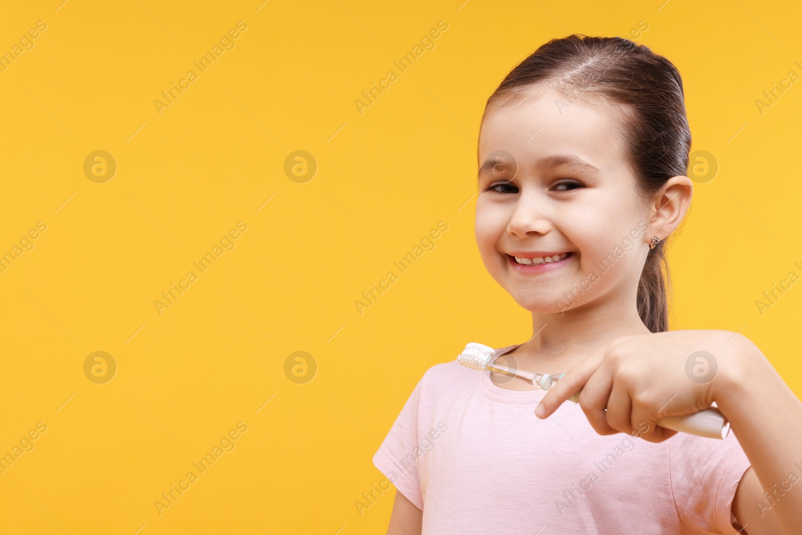 Photo of Cute girl with toothbrush on orange background, space for text