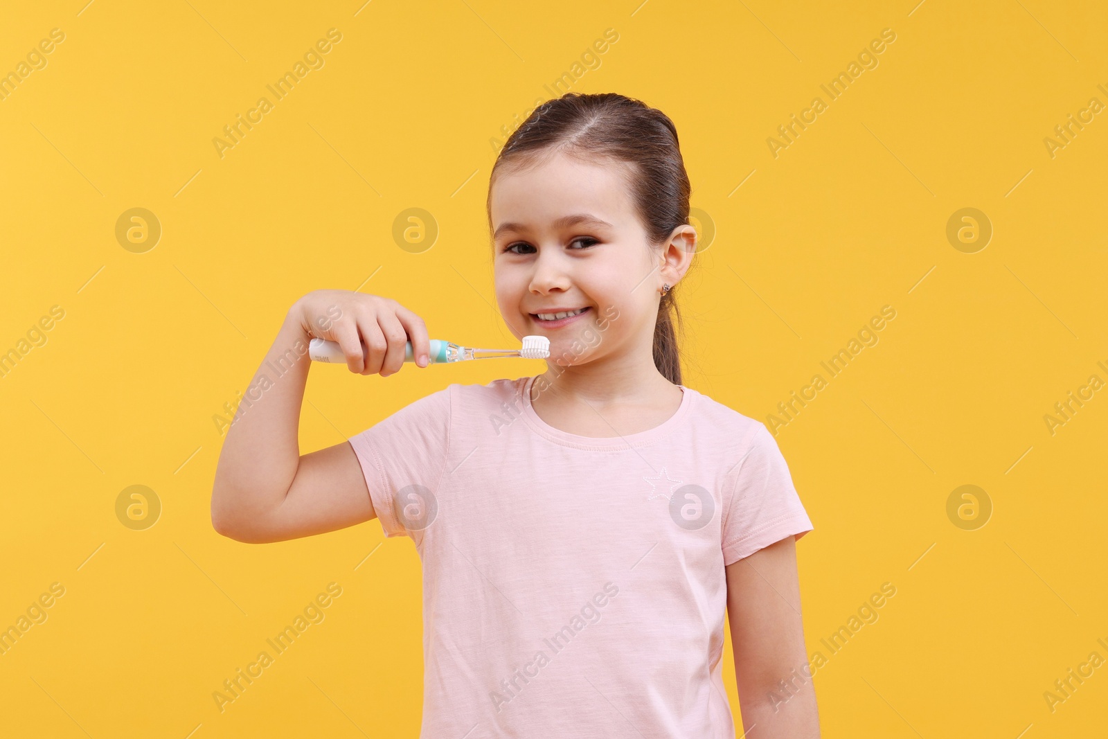 Photo of Cute girl with toothbrush on orange background