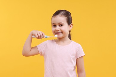 Photo of Cute girl with toothbrush on orange background