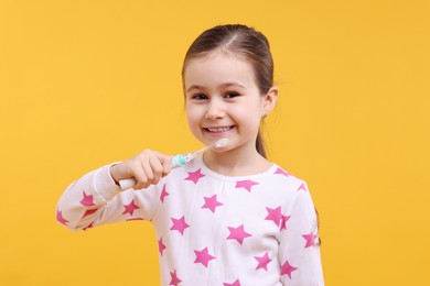 Photo of Cute girl with toothbrush on orange background