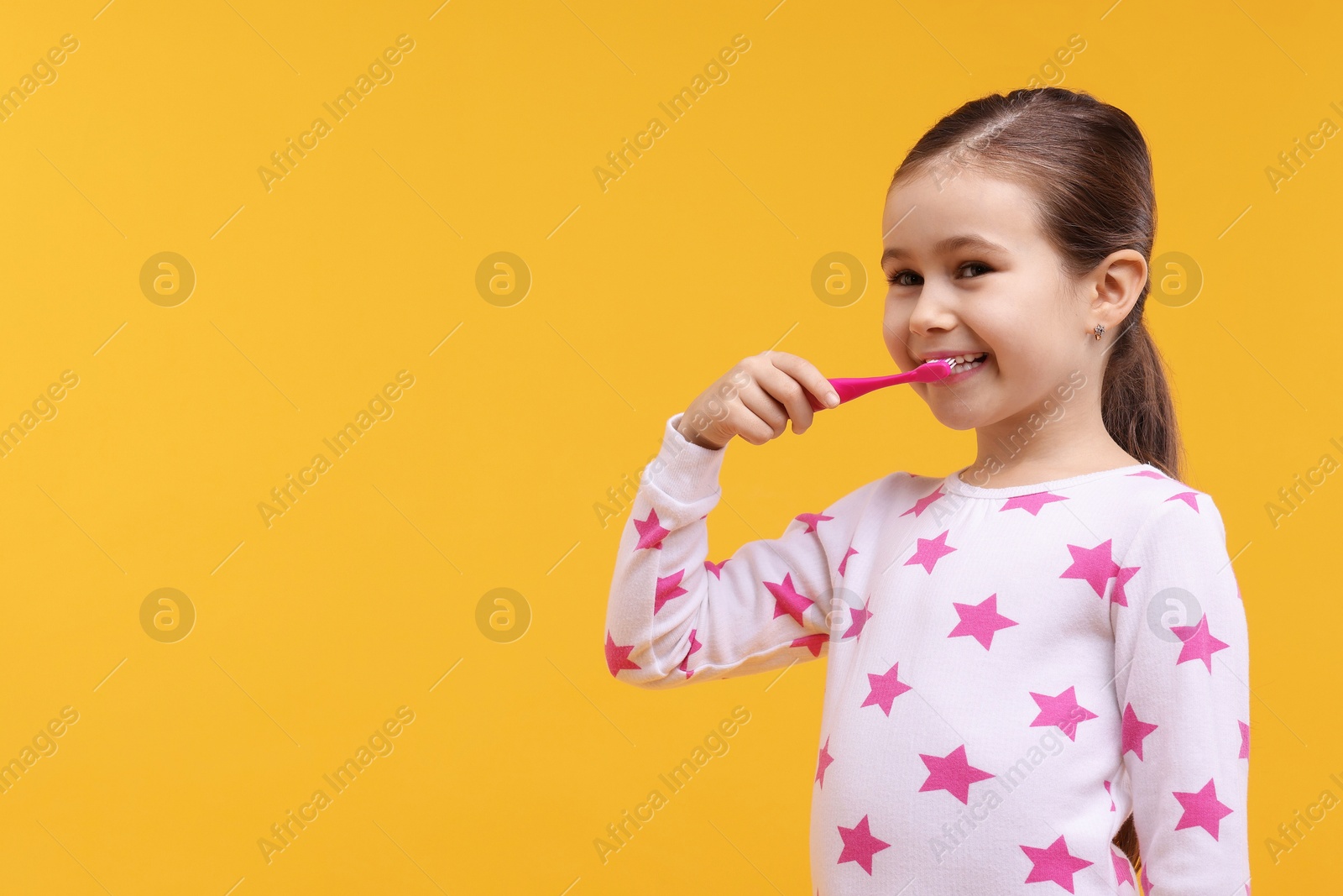 Photo of Cute girl brushing her teeth on orange background, space for text