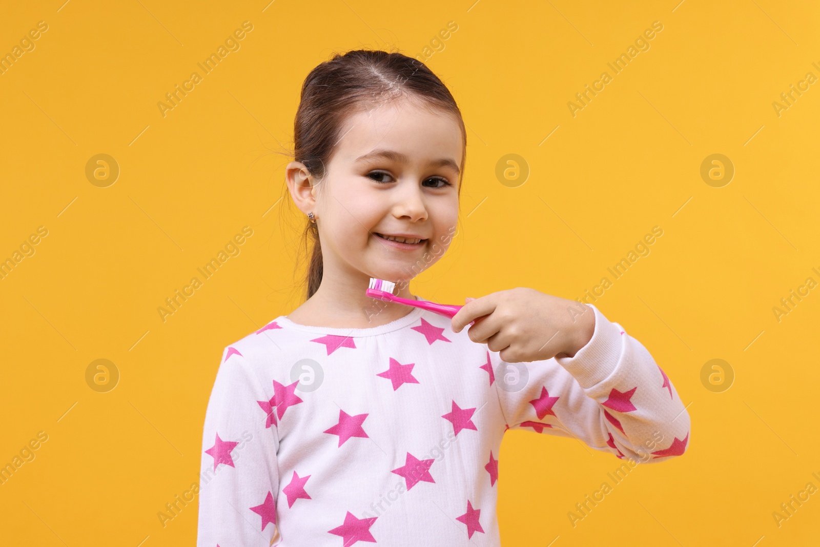 Photo of Cute girl with toothbrush on orange background