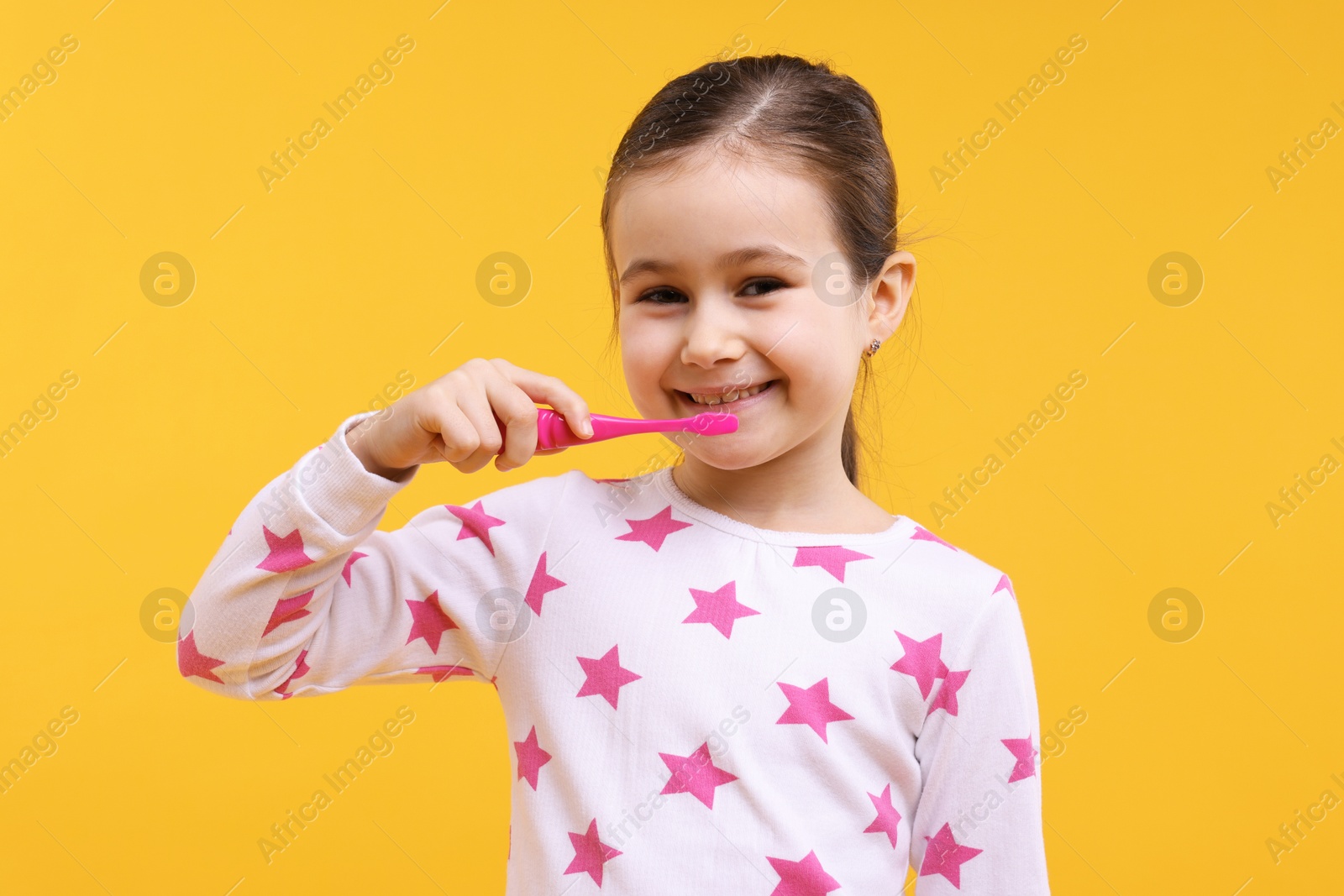 Photo of Cute girl brushing her teeth on orange background