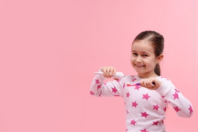 Photo of Cute girl applying toothpaste onto toothbrush on pink background, space for text