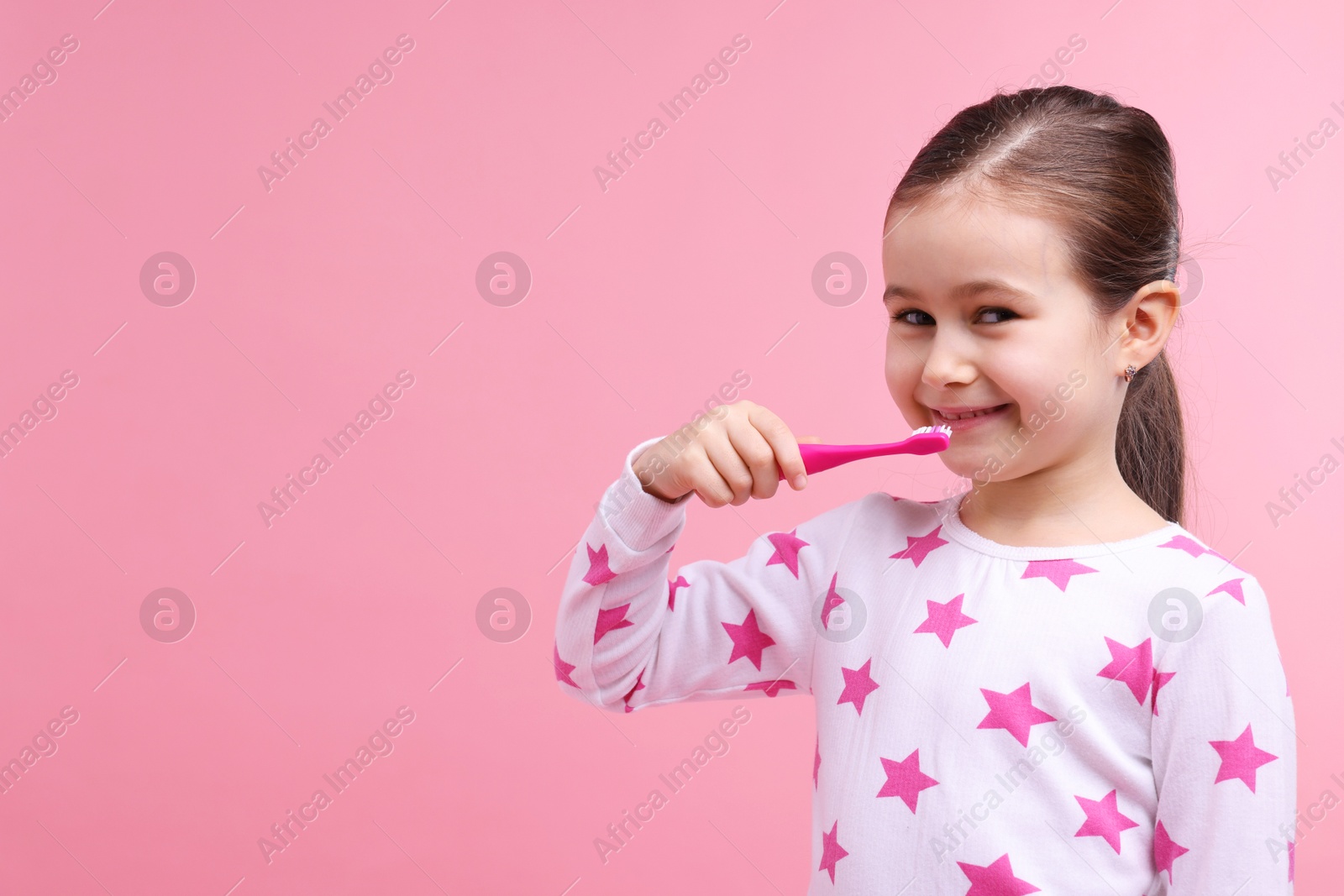 Photo of Cute girl brushing her teeth on pink background