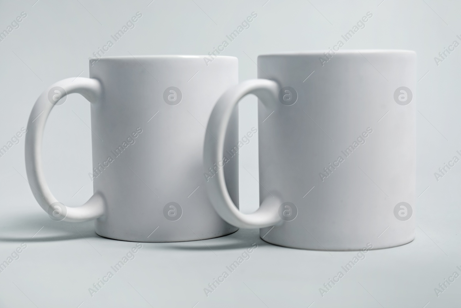 Photo of Two blank mugs for branding on light grey background. Mockup for design