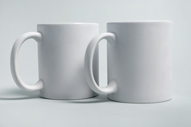 Photo of Two blank mugs for branding on light grey background. Mockup for design