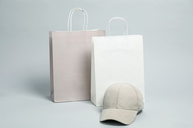 Photo of Blank paper shopping bags and cap for branding on light grey background. Mockup for design