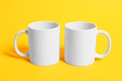 Photo of Two blank mugs for branding on orange background. Mockup for design