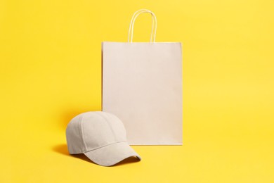 Photo of Blank paper shopping bag and cap for branding on orange background. Mockup for design