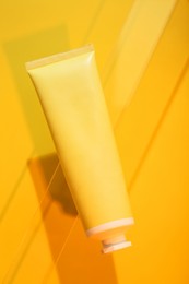 Tube of cream on orange background, top view. Stylish presentation of skincare product