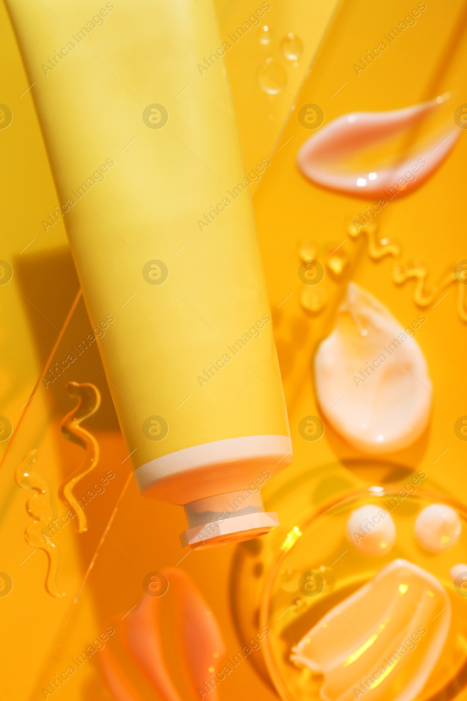 Photo of Cream and gel samples on orange background, flat lay. Stylish presentation with tube of skincare product