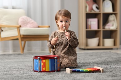 Photo of Cute little girl playing with toy musical instruments on floor at home