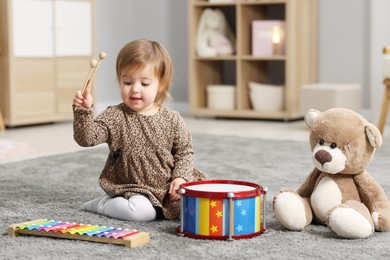 Photo of Cute little girl playing with toy musical instruments on floor at home