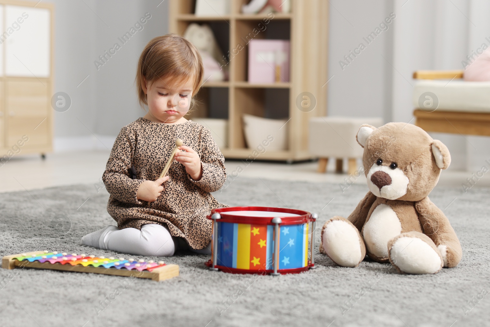 Photo of Cute little girl playing with toy musical instruments on floor at home