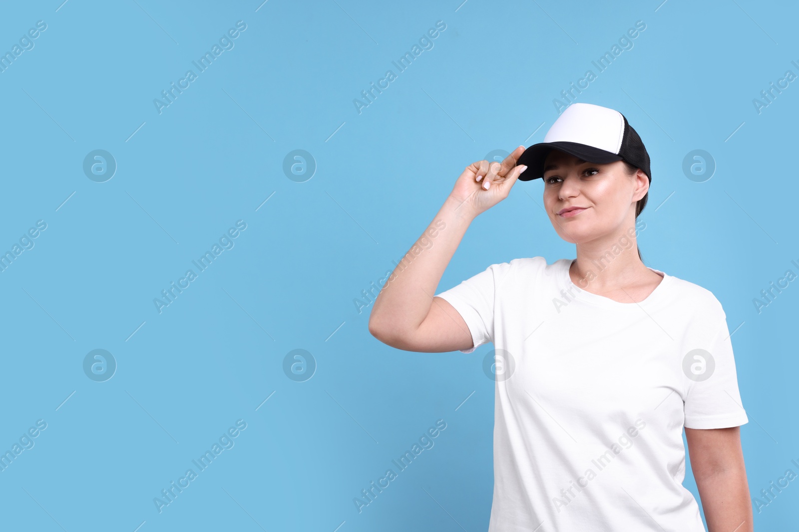 Photo of Woman in white t-shirt and baseball cap on light blue background. Mockup for design