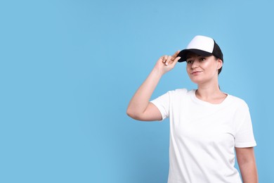 Photo of Woman in white t-shirt and baseball cap on light blue background. Mockup for design