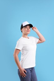 Photo of Woman in white t-shirt and baseball cap on light blue background. Mockup for design