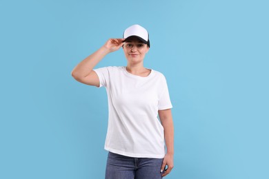 Photo of Woman in white t-shirt and baseball cap on light blue background. Mockup for design