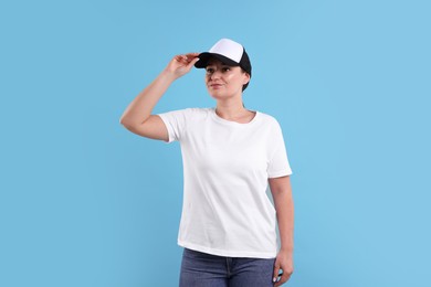 Photo of Woman in white t-shirt and baseball cap on light blue background. Mockup for design