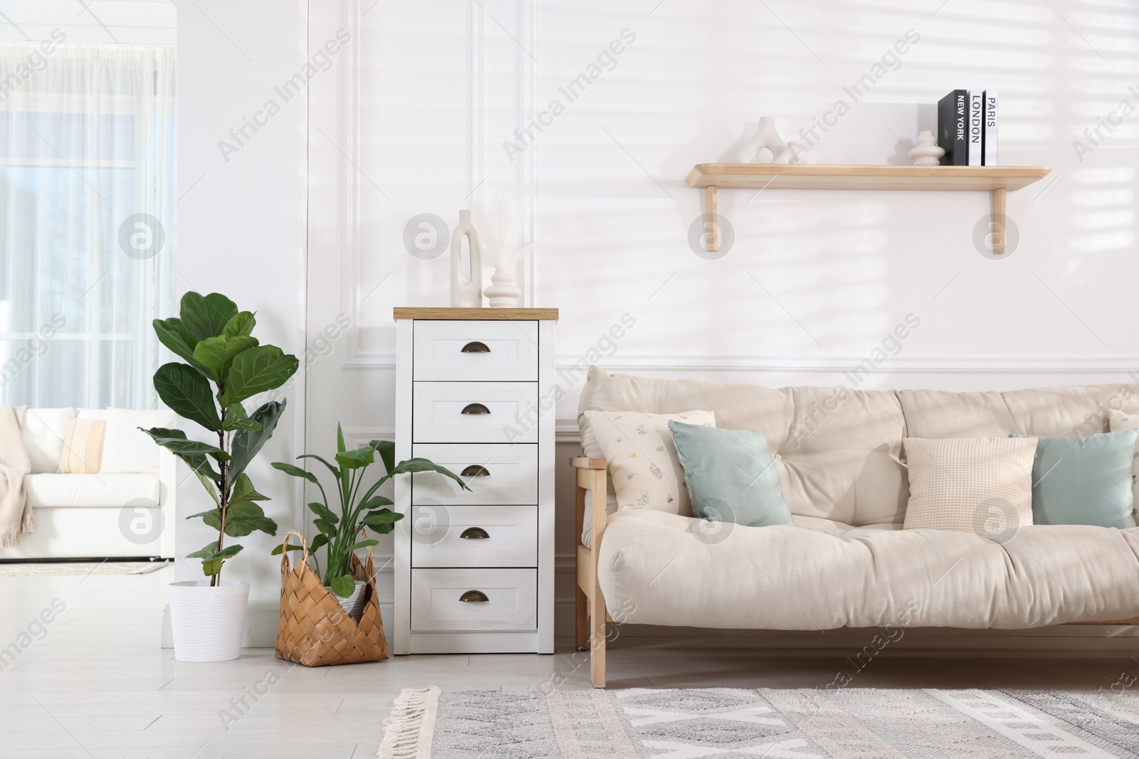 Photo of Beautiful sofa with cushions, commode and houseplants in living room. Interior design