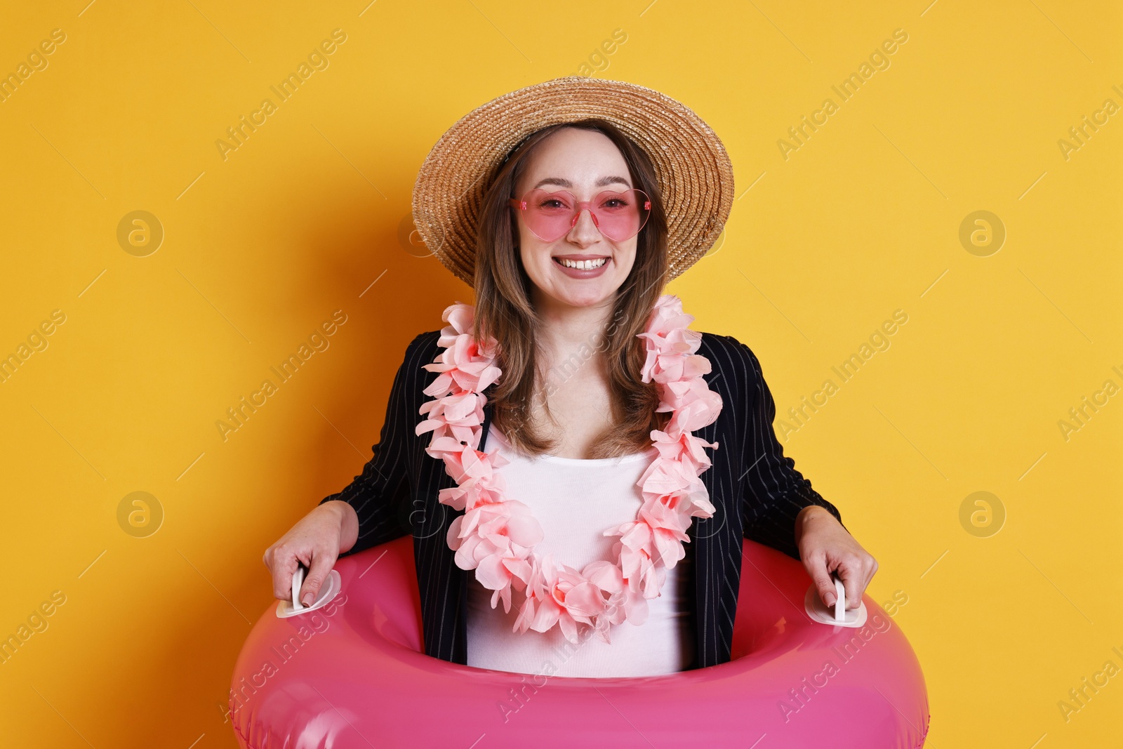 Photo of Businesswoman with inflatable ring, straw hat, flower wreath and sunglasses on orange background