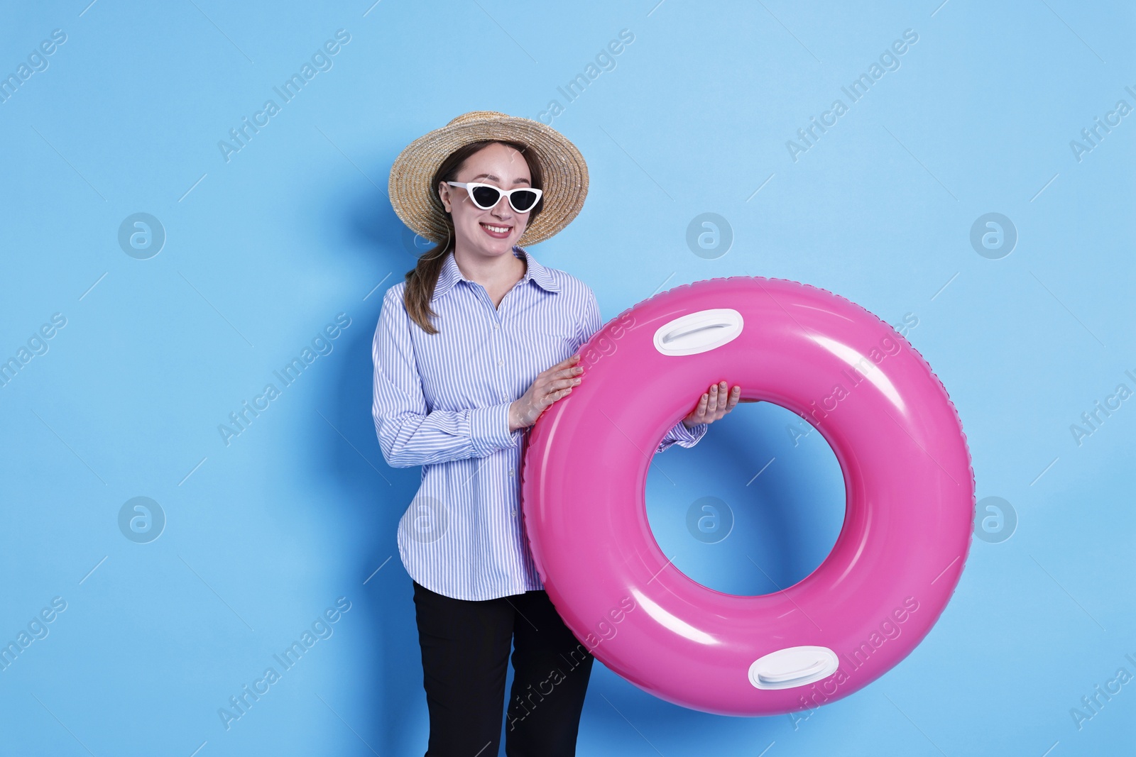 Photo of Businesswoman with inflatable ring, straw hat and sunglasses on light blue background