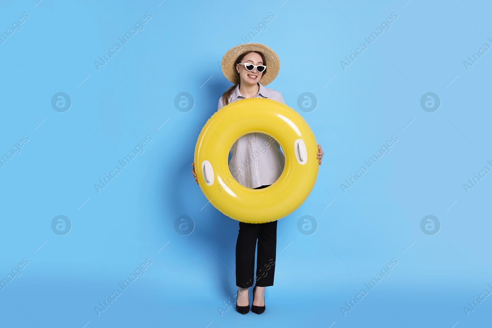 Photo of Businesswoman with inflatable ring, straw hat and sunglasses on light blue background